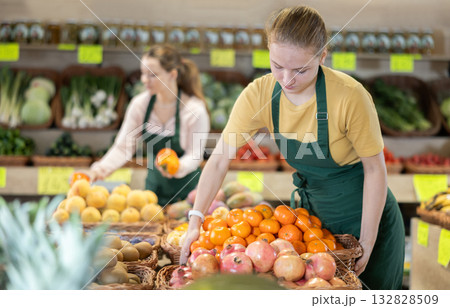 Girl employees in uniform holding mandarines in grocery shop Girl employees in uniform holding mandarines in grocery shop 132828509