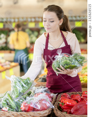 Young woman seller puts packaged peppers in store 132828515