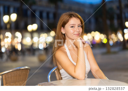 Woman sits at a table in a cafe overlooking the evening city of Barcelona Woman sits at a table in a cafe overlooking the evening city of Barcelona 132828537
