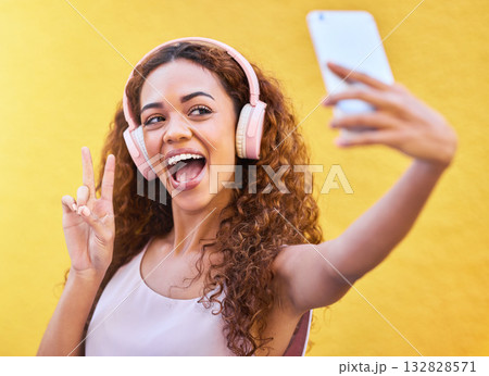 Black woman, peace selfie and music headphones on yellow wall background for freedom. Happy and excited gen z person outdoor listening to podcast audio with hand sign or emoji for influencer post 132828571
