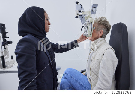 Eye exam, vision and woman with Muslim optometrist in clinic for test, eyesight and optical assessment. Optometry, healthcare and female optician with elderly patient, phoropter and medical tools Eye exam, vision and woman with Muslim optometrist in clinic for test, eyesight and optical assessment. Optometry, healthcare and female optician with elderly patient, phoropter and medical tools 132828762