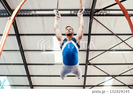 Man, acrobat and gymnastics swinging on rings in fitness for practice, training or workout at gym. Professional male gymnast hanging on ring circles for athletics, acrobatics or strength exercise Man, acrobat and gymnastics swinging on rings in fitness for practice, training or workout at gym. Professional male gymnast hanging on ring circles for athletics, acrobatics or strength exercise 132829145