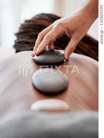 Black woman, hands and rock on back in spa treatment for relaxation, stress relief or massage at resort. Hand of masseuse applying rocks to African American female in physical therapy for wellness 132829185