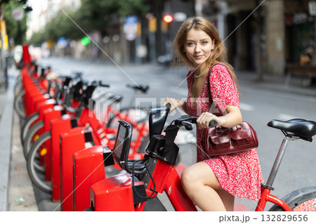 Woman in red dress rents electric bike on street of european city Woman in red dress rents electric bike on street of european city 132829656
