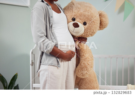 Pregnant, teddy bear and woman with hand on stomach for growth, development and bonding in room. Black person during pregnancy with stuffed animal toy for care, love and support for healthy lifestyle 132829683