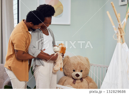 Love, teddy bear and pregnant couple in the nursery with excitement while preparing for their baby. Happy, pregnancy and young African man with his maternal wife looking at toy together in bedroom. 132829686