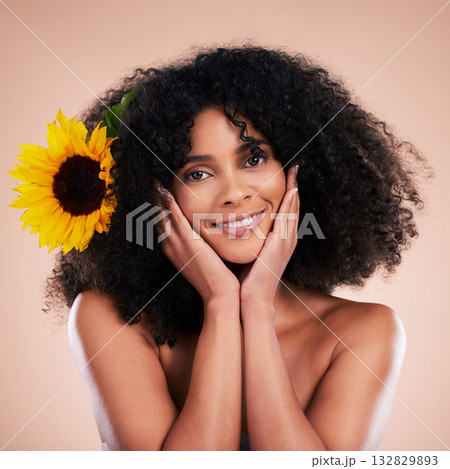 Black woman, studio portrait and sunflower with beauty, smile and cosmetic wellness by beige background. African gen z model, flower and spring aesthetic with hands, happy and natural makeup on face 132829893