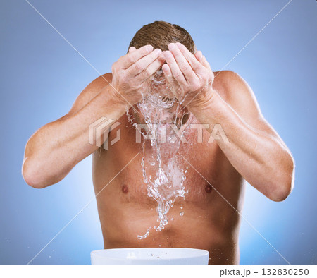 Man, water splash and face wash in skincare by basin for hygiene or natural sustainability against blue studio background. Male washing for clean health, wellness or self care for facial treatment Man, water splash and face wash in skincare by basin for hygiene or natural sustainability against blue studio background. Male washing for clean health, wellness or self care for facial treatment 132830250