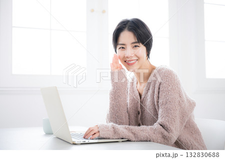 リビングでパソコンを使うニットを着た女性 カメラ目線で内緒話やコッソリ教えるのポーズ リビングでパソコンを使うニットを着た女性 カメラ目線で内緒話やコッソリ教えるのポーズ 132830688