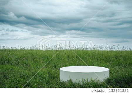 Minimalist Composition Featuring Large White Pedestal on Green Grass Under Cloudy Sky 132831822