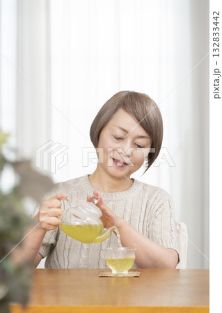 夏リビングで冷茶を飲むシニア女性 132833442