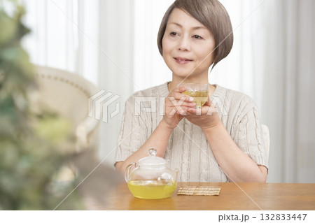 夏リビングで冷茶を飲むシニア女性 132833447