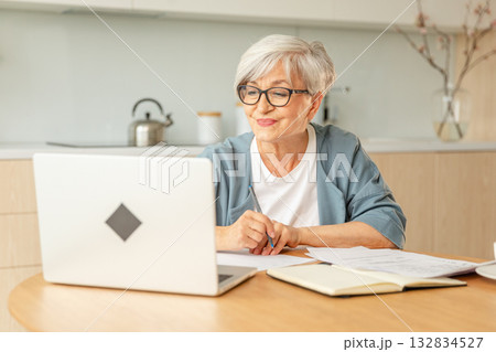 Online education courses webinar concept. Middle aged senior woman using laptop computer writing notes. Focused mature old woman enjoying studying online from home written records doing online work Online education courses webinar concept. Middle aged senior woman using laptop computer writing notes. Focused mature old woman enjoying studying online from home written records doing online work 132834527