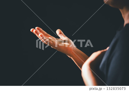 Dark silence of the church, a Christian lifts their hand in prayer to God, a symbol of worship, faith, and hope-embracing the spiritual concept of religion and believing in Jesus Christ. 132835073