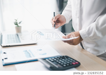 A businesswoman reviews financial report while holding documents and pointing with pen at office desk. Concept of accounting, budget management, financial analysis and corporate business planning. 132835152