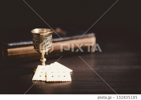 Holy communion bread and wine cup placed on the Holy Bible, symbolizing the Lord Supper, Eucharist, sacrifice of Jesus Christ, Christian worship and remembrance of faith. 132835185
