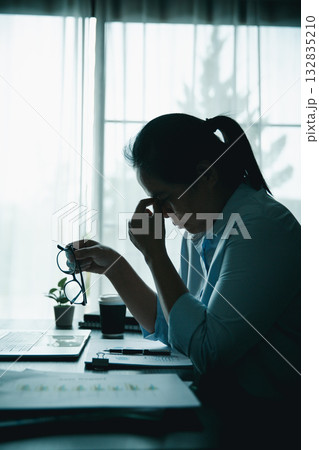 Stressed businesswoman working late at home office, feeling exhausted while reviewing financial documents on laptop. Concept of work stress, burnout, deadline, and overwork. 132835210