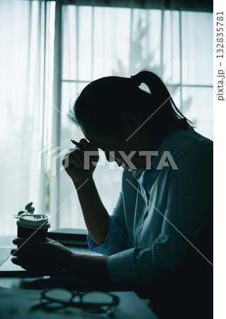 Stressed businesswoman working late at home office, feeling exhausted while reviewing financial documents on laptop. Concept of work stress, burnout, deadline, and overwork. 132835781
