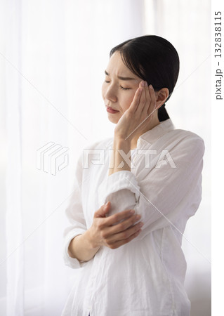 窓辺でこめかみに手を当て眉間に皺を寄せるミドル女性 窓辺でこめかみに手を当て眉間に皺を寄せるミドル女性 132838115