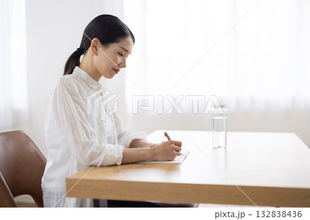 テーブルでノートにメモをとるミドル女性 テーブルでノートにメモをとるミドル女性 132838436