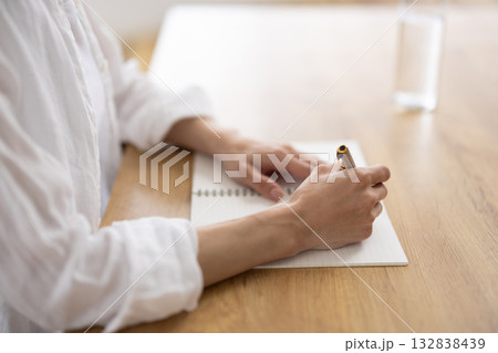 ノートに書き込む白いシャツの女性の手元 132838439
