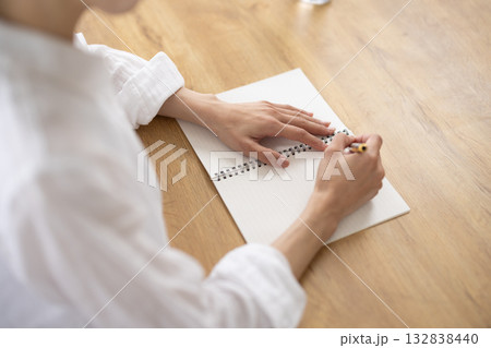 ノートに書き込む白いシャツの女性の手元 132838440