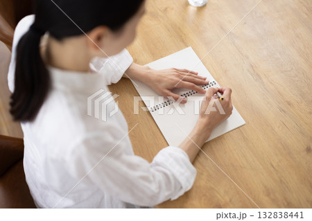ノートに書き込む白いシャツの女性の手元 132838441
