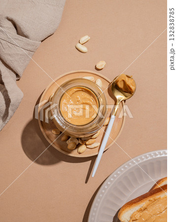 Peanut butter in a glass jar and spoon on a beige background with toast 132838785