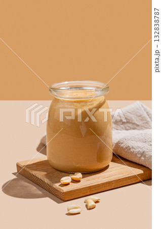 Peanut butter in a glass jar on a wooden board on a beige background 132838787