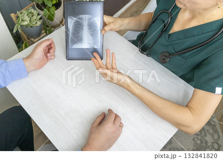 Shot of the female doctor in uniform showing x-ray image of the lungs on the tablet to the patient Shot of the female doctor in uniform showing x-ray image of the lungs on the tablet to the patient 132841820
