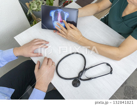 Shot of the female doctor in uniform showing x-ray image of the lungs on the tablet to the patient Shot of the female doctor in uniform showing x-ray image of the lungs on the tablet to the patient 132841821