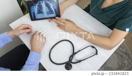 Shot of the female doctor in uniform showing x-ray image of the lungs on the tablet to the patient Shot of the female doctor in uniform showing x-ray image of the lungs on the tablet to the patient 132841823