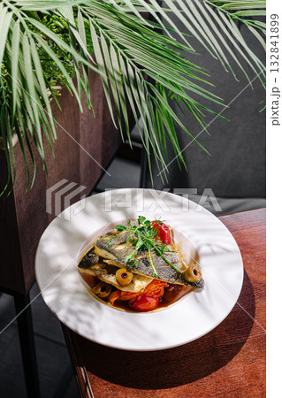 Grilled fish served with vegetables and herbs in a modern dining setting 132841899