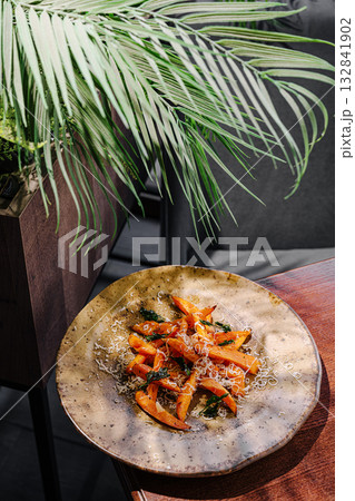 A plate of roasted orange vegetables garnished with herbs sits on a wooden table 132841902