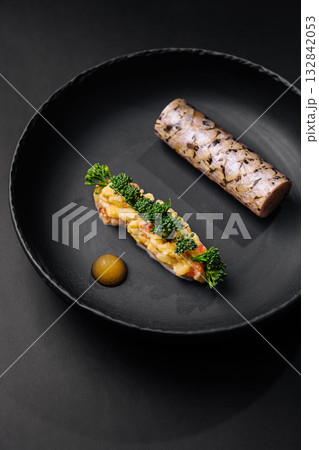 Gourmet dish featuring seafood and vegetable garnishes on a black plate 132842053