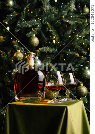 A rich bottle of whiskey sits on a green tablecloth next to two elegant glasses A rich bottle of whiskey sits on a green tablecloth next to two elegant glasses 132842073