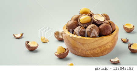 Macadamia nut with cracked nuts in wood bowl on pastel green background, closeup 132842182