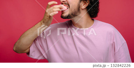 Man enjoying sweet dessert while smiling against a pink background Man enjoying sweet dessert while smiling against a pink background 132842226