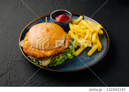 Crispy chicken burger served with golden fries and ketchup on a black plate 132842285