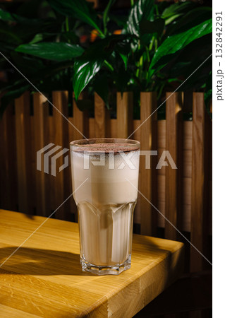 Elegant glass of creamy beverage on wooden table among green plants Elegant glass of creamy beverage on wooden table among green plants 132842291