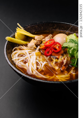 Flavorful bowl of steaming noodle soup with fresh garnishes and spices 132842335