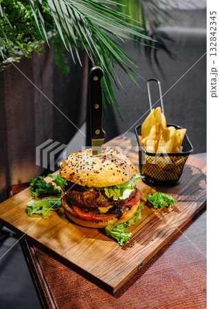 Juicy burger with fries served on a wooden board in a cozy setting Juicy burger with fries served on a wooden board in a cozy setting 132842345