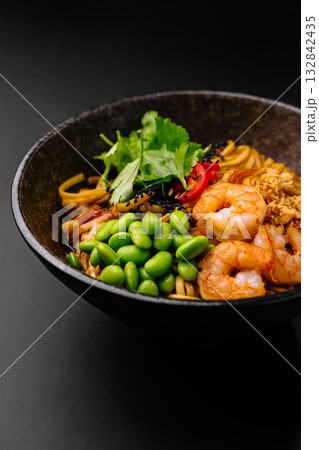 Delicious bowl of shrimp and noodle dish with fresh vegetables and toppings 132842435