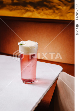 Refreshing pink drink served in a clear glass with foam and a flower garnish 132842522
