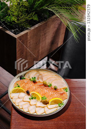 Assorted fish platter with salmon, white fish, lemon slices, and olives served on a wooden table in a restaurant. 132842579