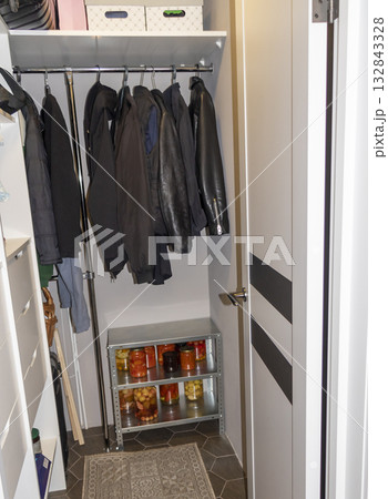 Wardrobe room with clothing, galvanized steel shelving unit with jar with different types of pickles and preserves on it. 132843328