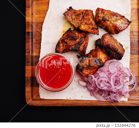 Savory grilled meat with spicy sauce and sliced onions on a wooden platter 132844276
