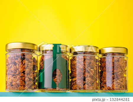 Jars filled with granola stand against a vibrant yellow backdrop 132844281