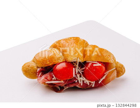 Croissant sandwich filled with ham, tomatoes, and cheese on a white plate 132844298