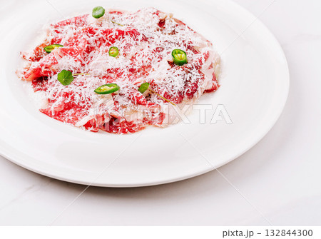 Slices of raw beef with cheese and green peppers served on a white plate Slices of raw beef with cheese and green peppers served on a white plate 132844300